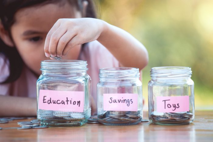 Young girl putting money into jar labelled education